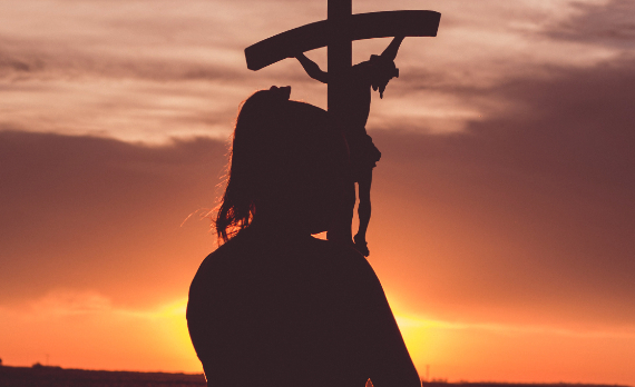 Una chica porta un crucifijo en alto al amanecer